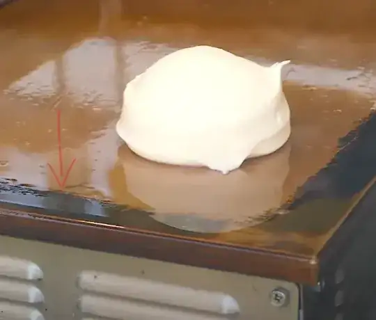 screen capture from pancake video with red arrow pointing to tarnish along edge of griddle