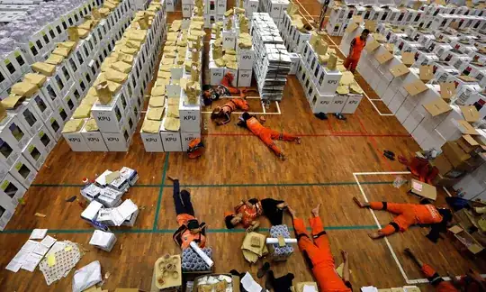 The caption reads: “Workers lie down during a break as they prepared election materials in a warehouse in Jakarta on 15 April.”